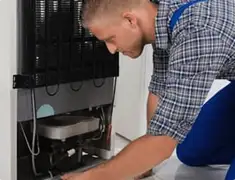 Refrigerator repair technician servicing the compressor and condenser area in Phoenix, AZ