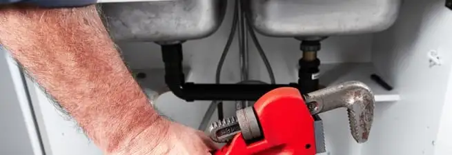 Garbage disposal repair technician tightening drain connections under a kitchen sink in Phoenix, AZ