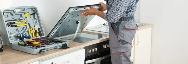 Cooktop repair technician lifting a built-in stovetop for service in Phoenix, AZ