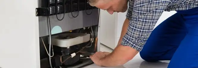 Refrigerator repair technician servicing the compressor and condenser area in Phoenix, AZ